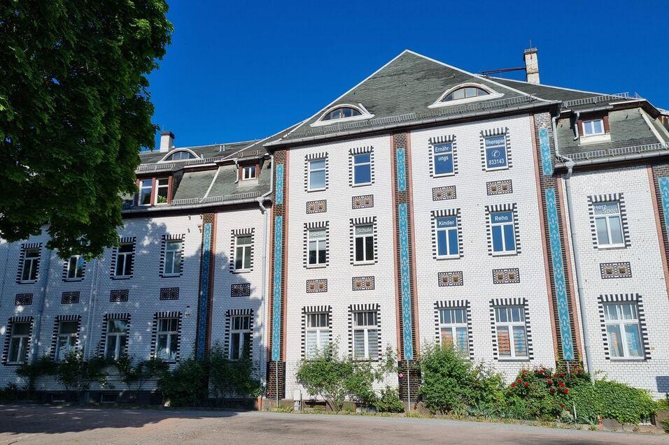 Fassade eines historischen Geb&auml;udes mit Fenstern und bunten Verzierungen, umgeben von Gr&uuml;nanlagen und blauem Himmel.