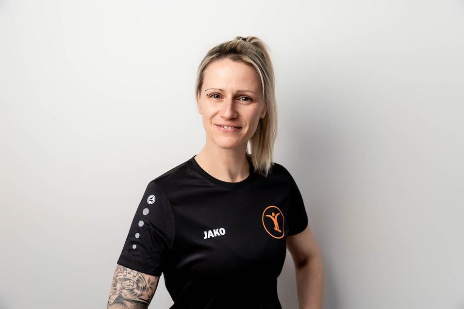 Portr&auml;t einer l&auml;chelnden Frau mit blonden Haaren, die ein schwarzes Sporttrikot mit dem Logo &bdquo;JAKO&ldquo; tr&auml;gt.