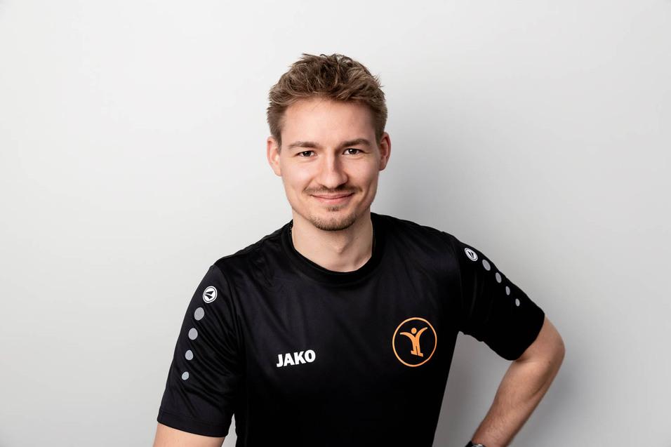 L&auml;chelnder Mann in schwarzem Sportshirt mit "JAKO"-Logo steht vor einem neutralen Hintergrund.