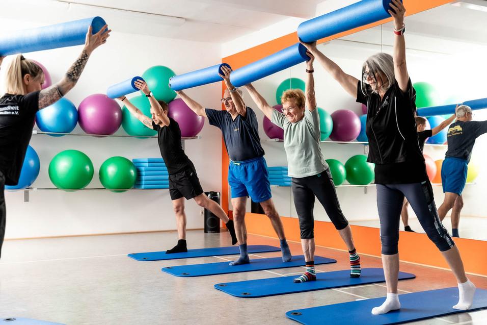 Gruppe von vier Personen beim Fitness-Training mit blauen Schaumstoffrollen auf Yogamatten in einem modernen Raum.